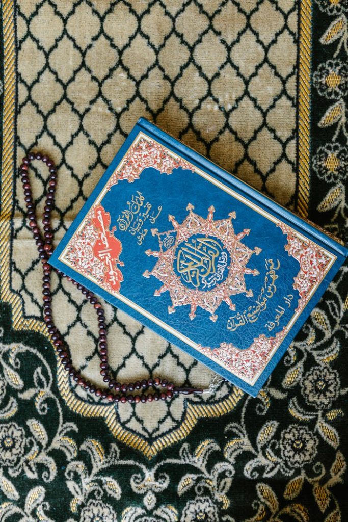 Top view of a Quran with prayer beads on a decorative Islamic carpet.
