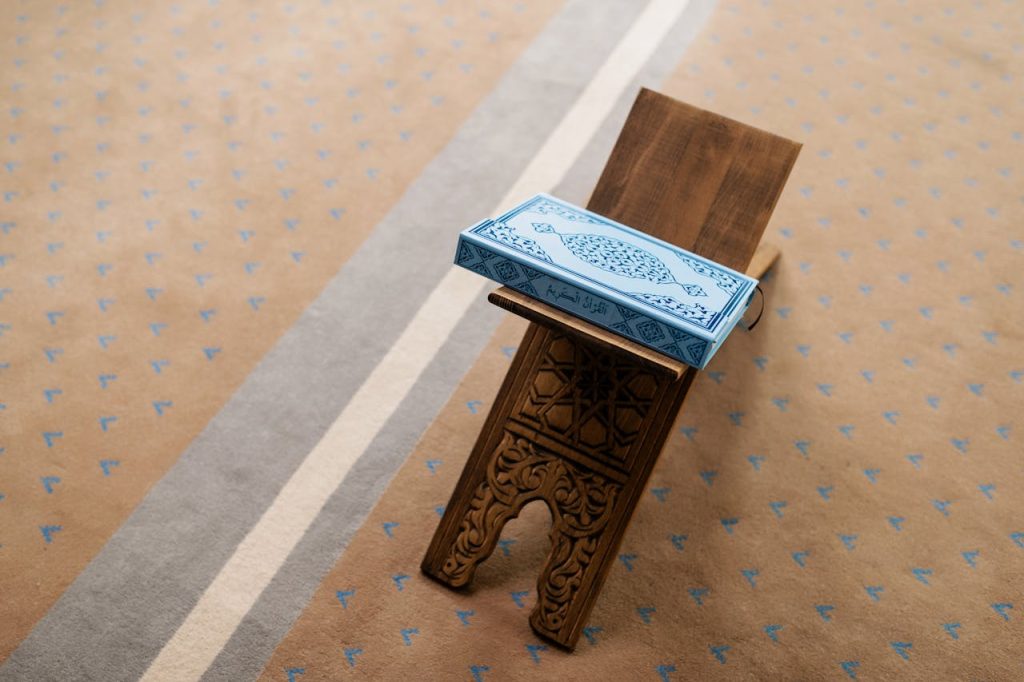 koran-on-table-in-mosque-8164394 A Quran placed on an intricately carved wooden stand in a mosque setting.